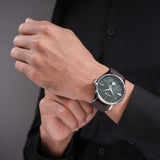 Silver-toned watch with a round case, green dial with radiating texture, white markers, and a brown leather strap.