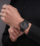 Gun-toned watch with a black textured dial, silver-toned hands and markers, and a black leather strap.