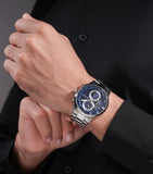 Silver-toned watch with a dark bezel, blue textured dial, three silver-toned sub-dials, and a multi-link metal bracelet.