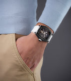 Angular gunmetal-toned skeleton watch with a dark blue dial, exposed gears, and a white silicone strap.
