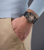 Black irregular-shaped watch with a skeleton dial, rose gold-toned accents, and a black ribbed silicone strap.