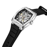Silver-toned tonneau steel watch with a black skeleton dial revealing gears, on a black ribbed silicone strap with a silver-t