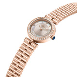 Rose gold-toned watch with a pink mother-of-pearl sunray dial, clear stone bezel, blue crown, and a three-link bracelet.
