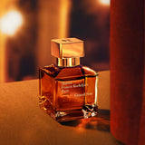 Clear rectangular glass perfume bottle with amber liquid, a square gold-toned cap with an embossed logo, and a white text lab