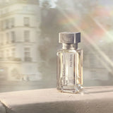 Clear glass rectangular perfume bottle with beveled edges, silver-toned neck, and a gray marble-patterned square cap. Labeled