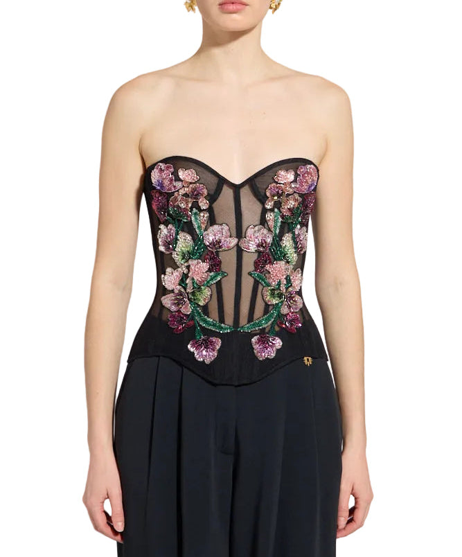 Black strapless corset top with sheer mesh and multi-colored beaded floral embroidery. Black pleated trousers.