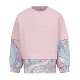 Pink crewneck sweatshirt with dropped shoulders and wide cuffs, layered over a long-sleeved shirt with a swirling pink, blue,