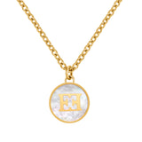 A detailed macro studio photograph focusing on the central medallion of the Escada Caroline necklace, highlighting the iridescent white Mother of Pearl inlay beneath the high-shine gold-plated EE logo crest.