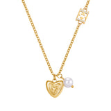 A high-detail close-up shot of the Escada Mina pendant assembly, highlighting the polished concentric lines of the gold heart, the swinging round white pearl, and the crystal-pave borders on the upper monogram logo link.