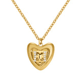 A high-detail close-up shot of the Escada Mina heart pendant, focusing on the polished gold contours, the central back-to-back EE logo, and the flanking columns of white pave crystals.