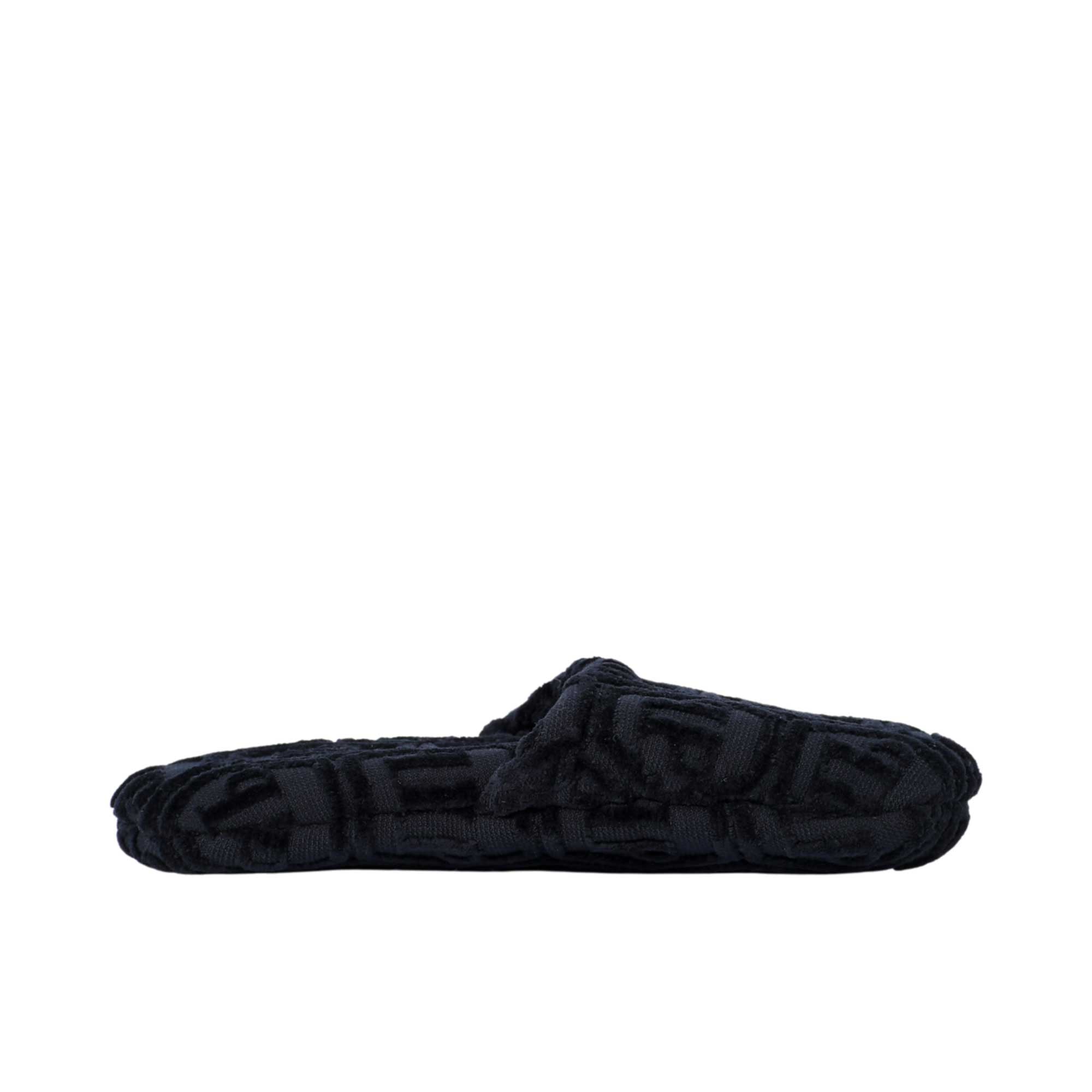 A BLACK terry cotton slipper is shown in a side profile view, highlighting the open-back and the hexagonal logo pattern on the fabric.