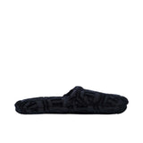 A BLACK terry cotton slipper is shown in a side profile view, highlighting the open-back and the hexagonal logo pattern on the fabric.