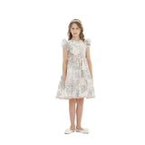 A young girl standing against a white background wearing a cream-colored knee-length party dress with a dusty rose botanical floral print, ruffled sleeves, and a matching pink headband.