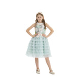 A young girl in a mint green tiered tulle party dress with a silver sequined floral bodice and a matching peach bow headband, posing against a white background.