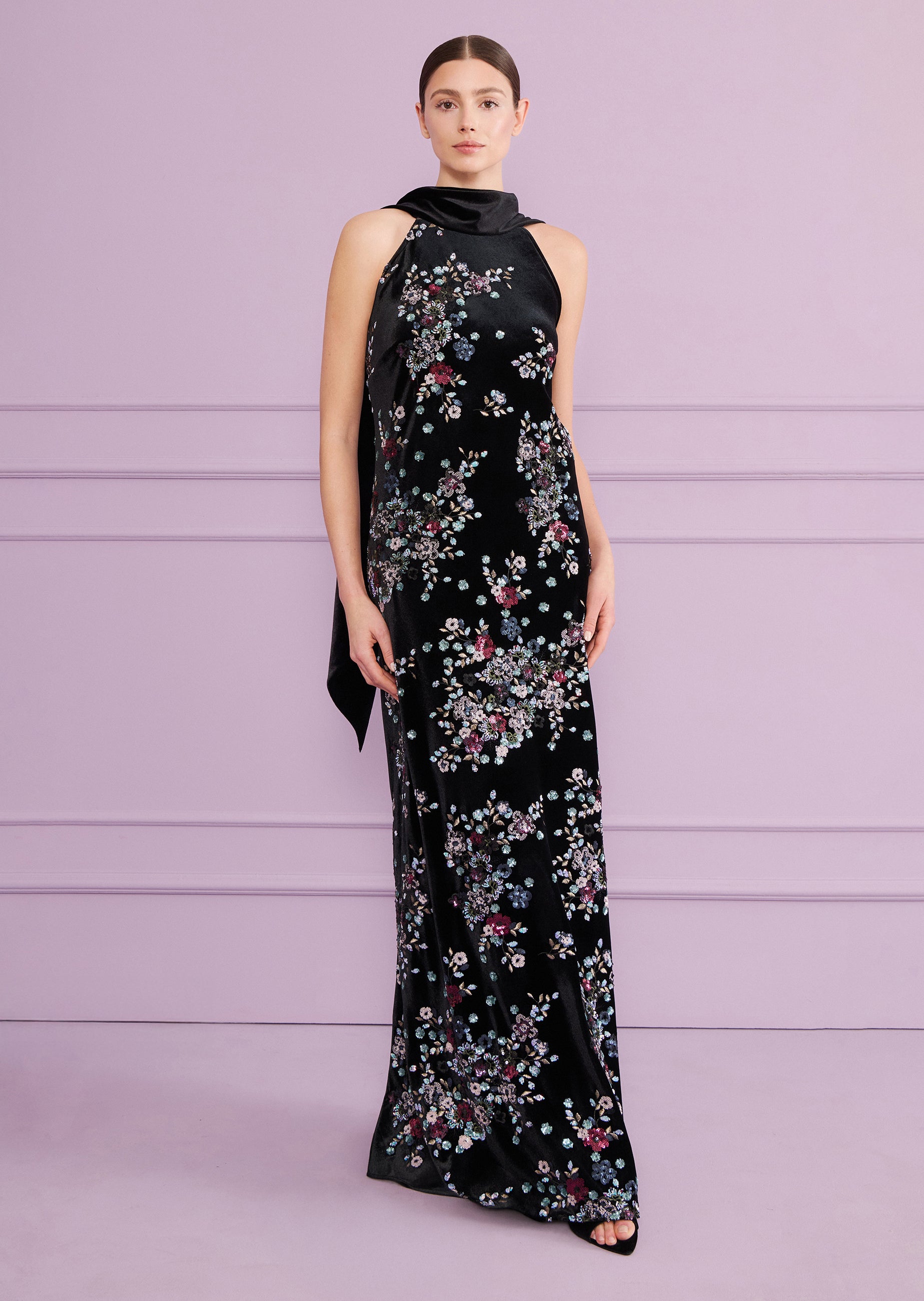 Black velvet long dress with a cowl halter neck and a long tie detail, covered in a colorful floral pattern.