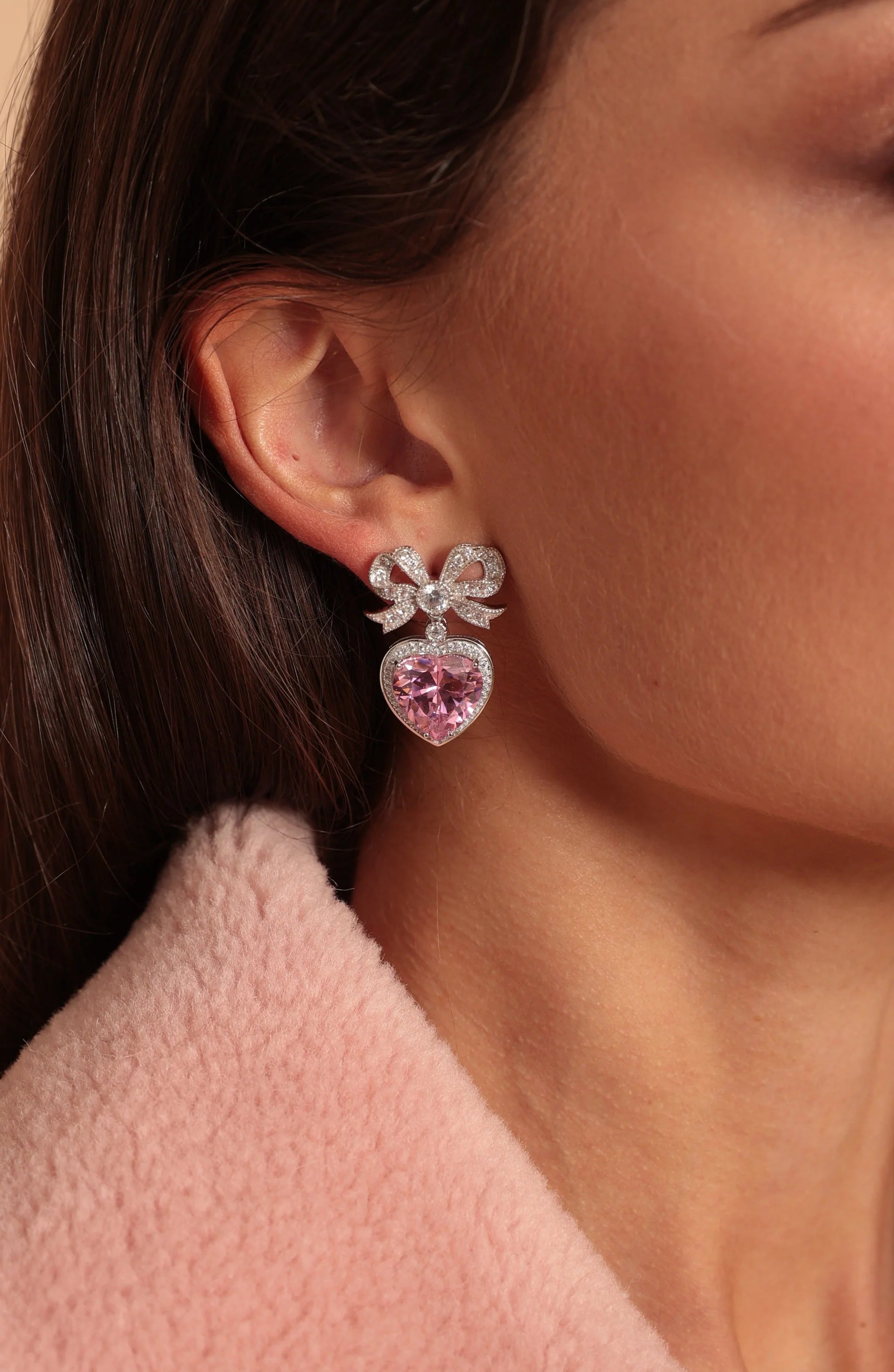 Silver-toned earring with a crystal-studded bow, a single clear crystal, and a pink crystal heart framed by small crystals.