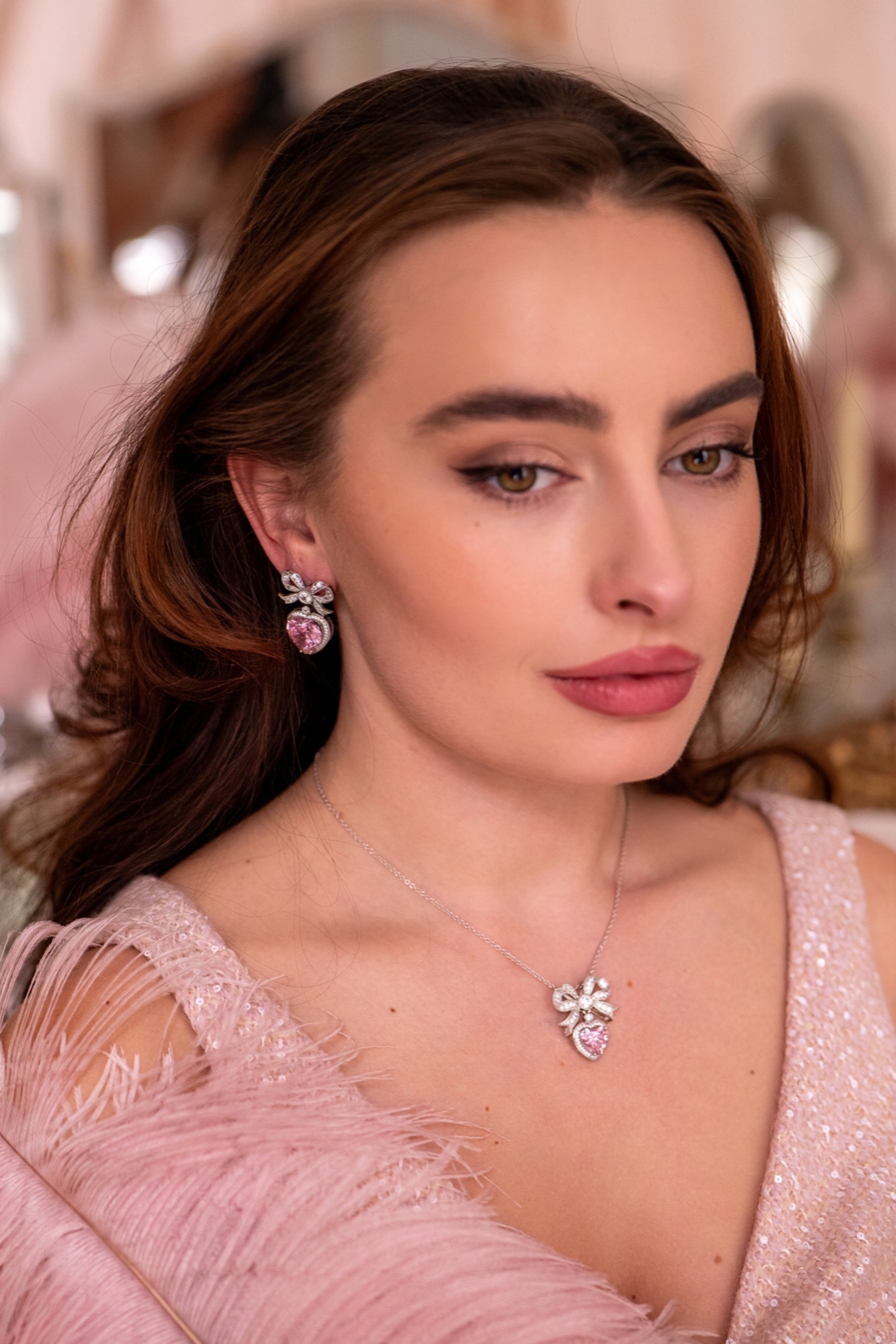 One silver-toned earring features a crystal-studded bow with a dangling pink crystal heart, also studded with crystals.