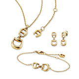 A professional studio display of the gold-plated Aigner Sella stainless steel jewelry set, highlighting the pendant necklace, chain bracelet with miniature logo charm, and matching drop earrings arranged together on a clean white background.