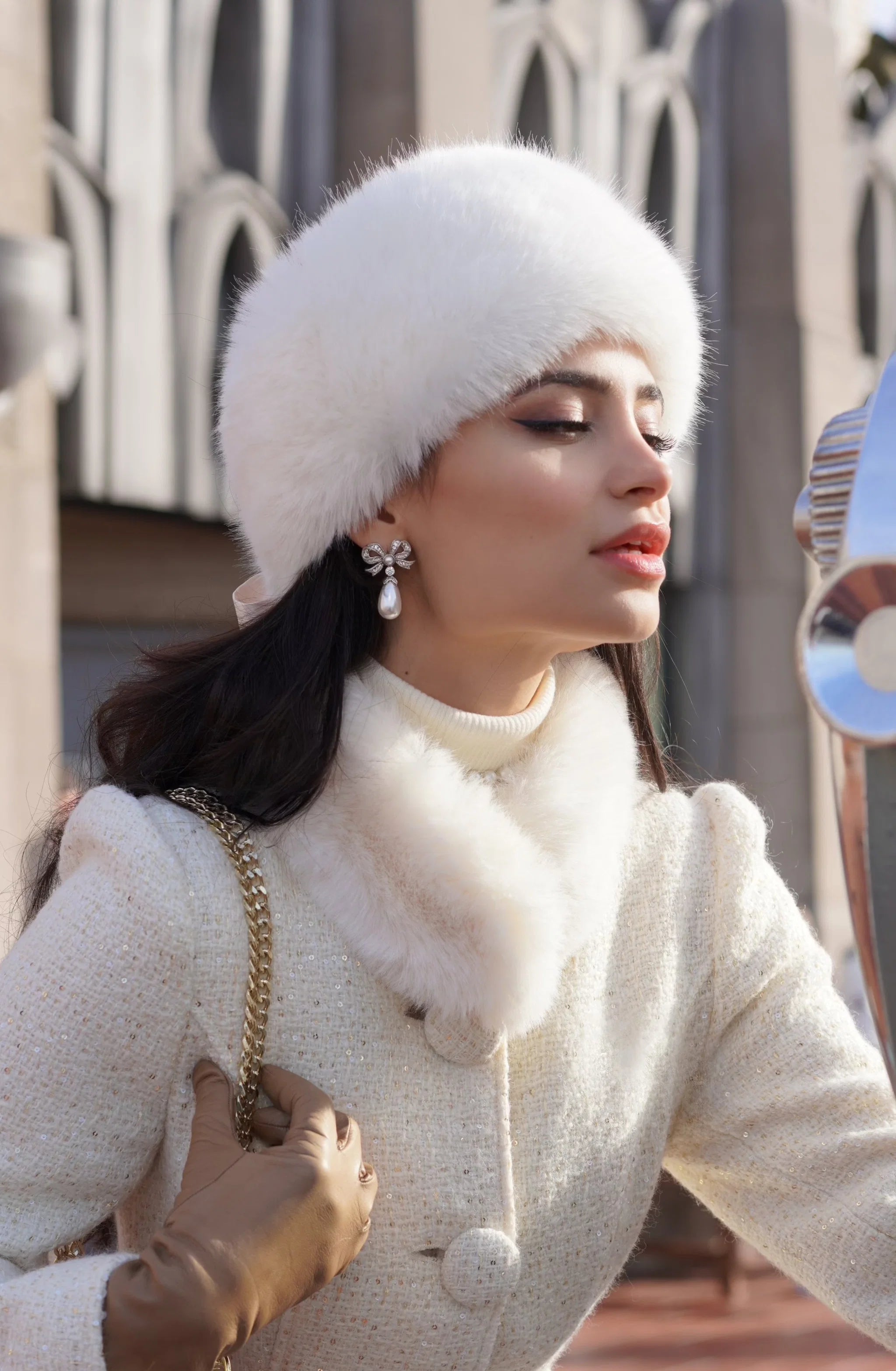 A silver-toned bow-shaped earring with clear stones and a dangling white teardrop pearl.