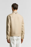 Beige pure linen gabardine overshirt, back view. Features a collar, back yoke, dark neck label, and buttoned cuffs.