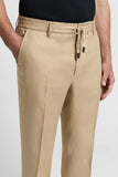Beige pure linen gabardine trousers with a flat front, belt loops, drawstring waist with black-tipped ends, and side pockets.