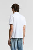 White piquet polo shirt, back view. Short sleeves with grey trim on cuffs. Features a collar and small side slits at the hem.