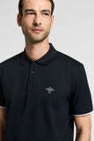 Dark blue pique polo shirt with a classic collar, three dark brown buttons, and a white embroidered logo on the chest. Short