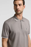 Taupe piquet polo shirt with short sleeves, collar, quarter-zip placket, white cuff trim, and embroidered chest logo.