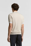 Beige pure cotton short-sleeved polo sweater, seen from the back, with a ribbed collar, ribbed cuffs with light grey trim, an