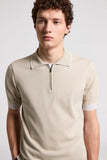 Beige pure cotton knit polo with white-trimmed collar, quarter-zip, and white-trimmed ribbed short sleeves.