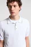 White pure cotton short-sleeved polo sweater with a textured knit, two light-toned buttons, and a dark stripe on the collar.