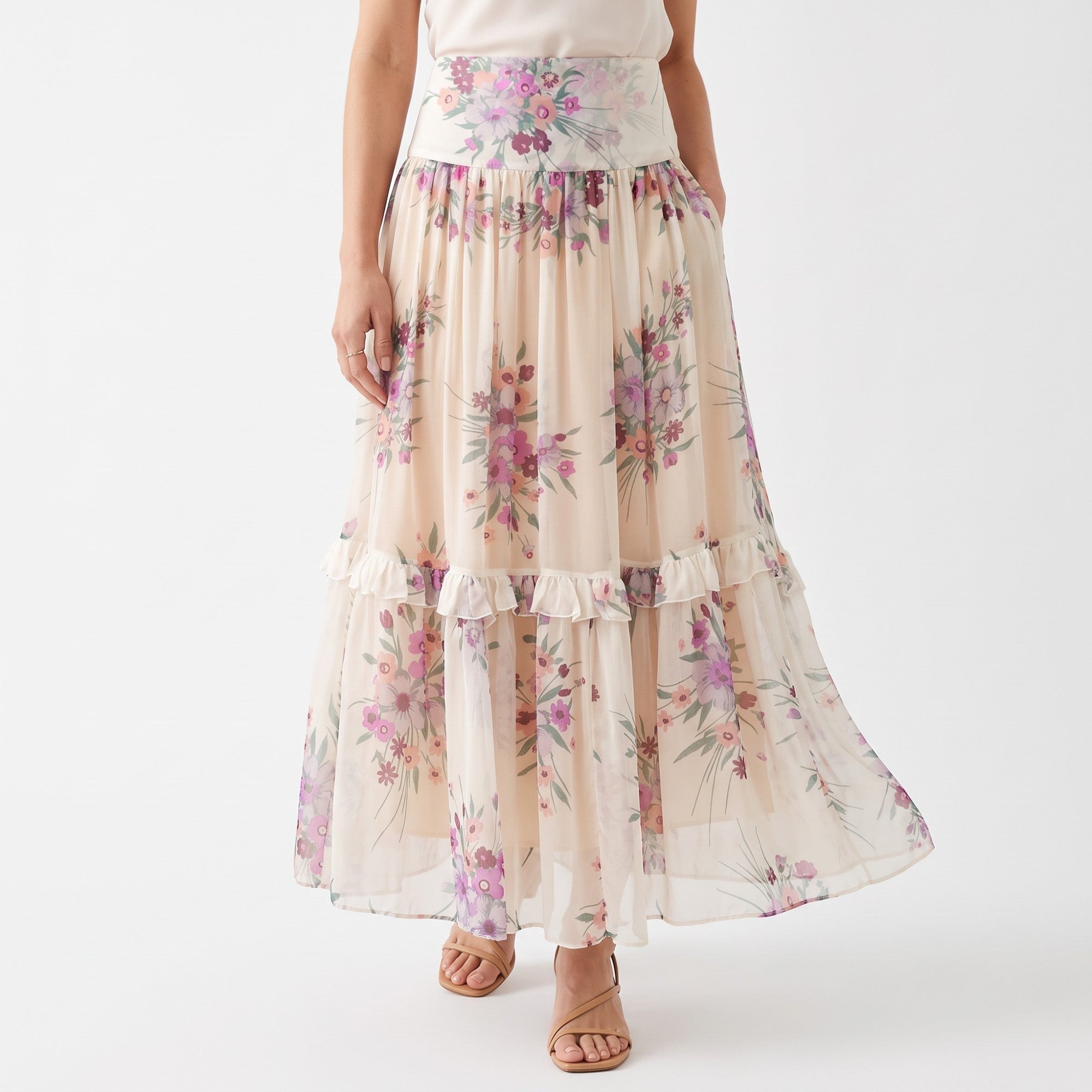 Long, flowing cream skirt with a wide waistband, all-over lilac and purple floral print, ruffled tier, and pockets.