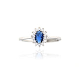 Silver-toned ring with a central oval dark blue stone surrounded by a halo of small clear stones on a thin band.