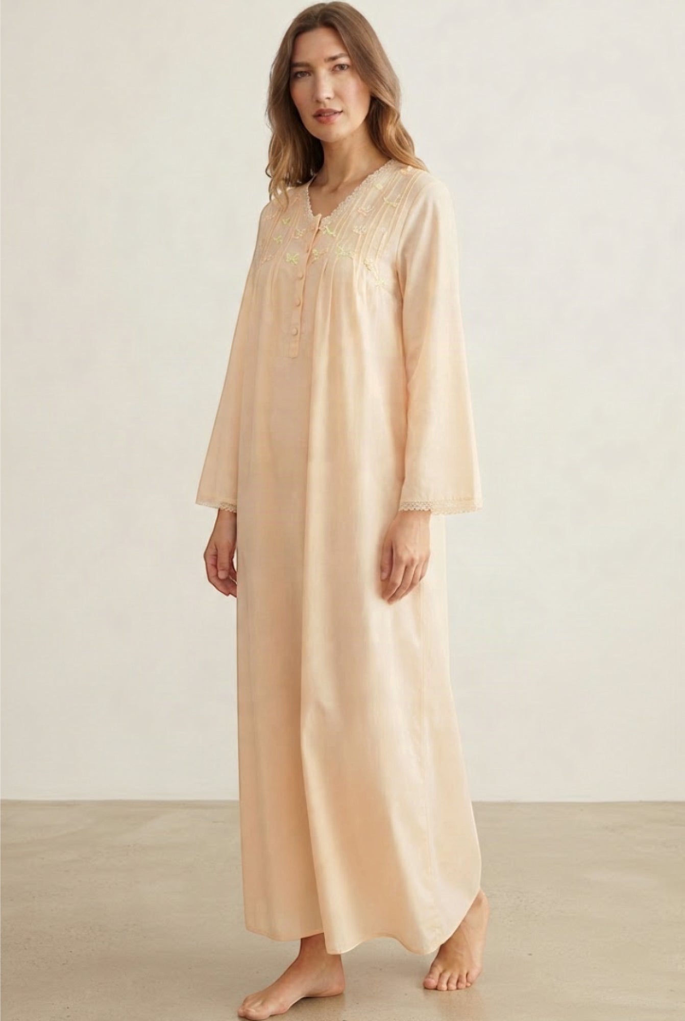 Long beige cotton abaya with V-neck, partial button placket, light yellow and green embroidery, and lace trim on cuffs.