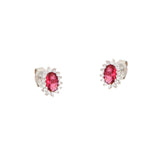 Pair of silver-toned stud earrings, each featuring an oval ruby-red central stone surrounded by a halo of clear faceted stone