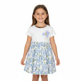 Front view of a young smiling girl with long straight brown hair modeling the Roberto Cavalli short-sleeved white and blue hydrangea dress against a plain white background.