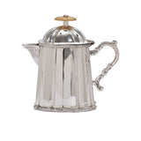 Close-up of a small silver-plated creamer pitcher with a hinged lid and decorative carvings.