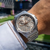 Silver-toned angular watch with a gray brushed dial, gold-toned hands and markers, three subdials, and a metal link bracelet.
