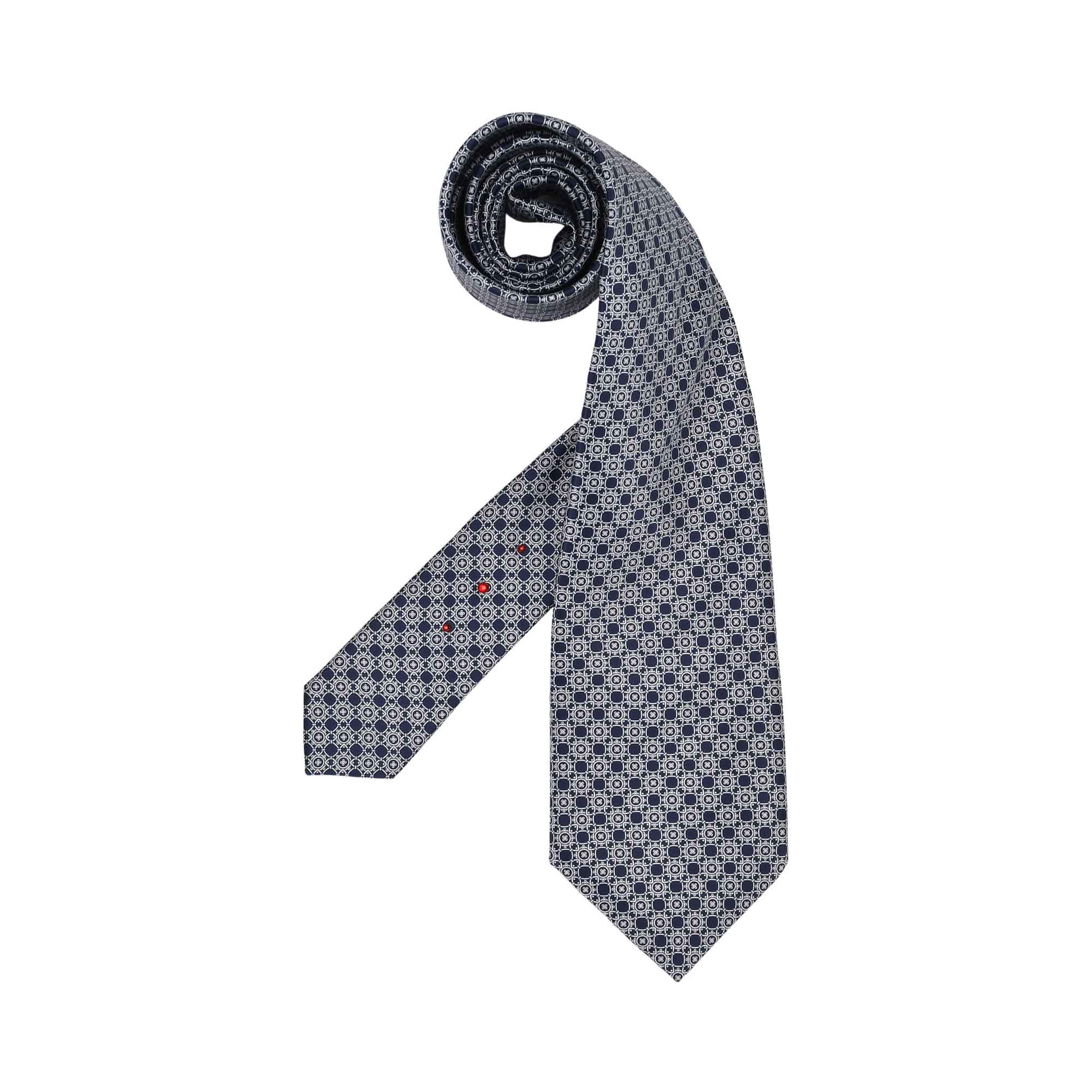 Navy blue and light blue geometric patterned tie, partially rolled. Three small red dots adorn the narrow end.