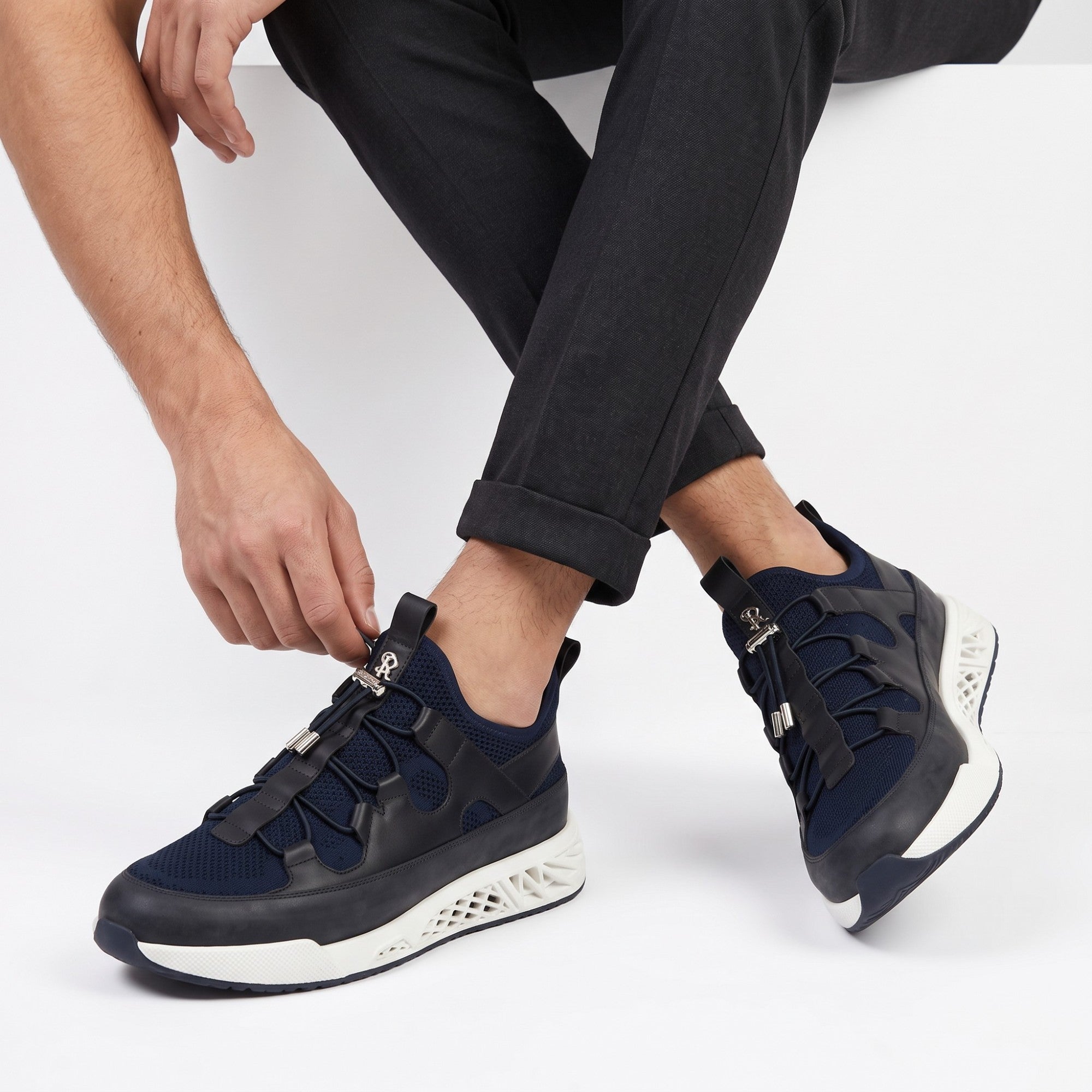 Navy blue mesh and black leather-like sneakers with elastic laces, silver-toned toggles, and a white geometric lattice sole.