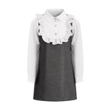 Black pinafore dress with thin straps over a white long-sleeved shirt featuring a ruffled front and heart-shaped buttons.