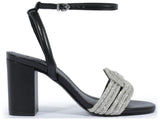 Side profile of a Schutz black leather block heel sandal featuring a silver crystal-encrusted knotted toe strap and adjustable ankle strap.
