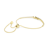 A side perspective studio shot of the Swarovski Mesmera bracelet draped on a white surface, highlighting the fluid movement of the delicate gold-tone chains and the polished spherical sliding closure.