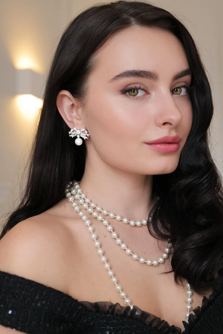 Silver-toned bow earring with clear stones and a white pearl drop.