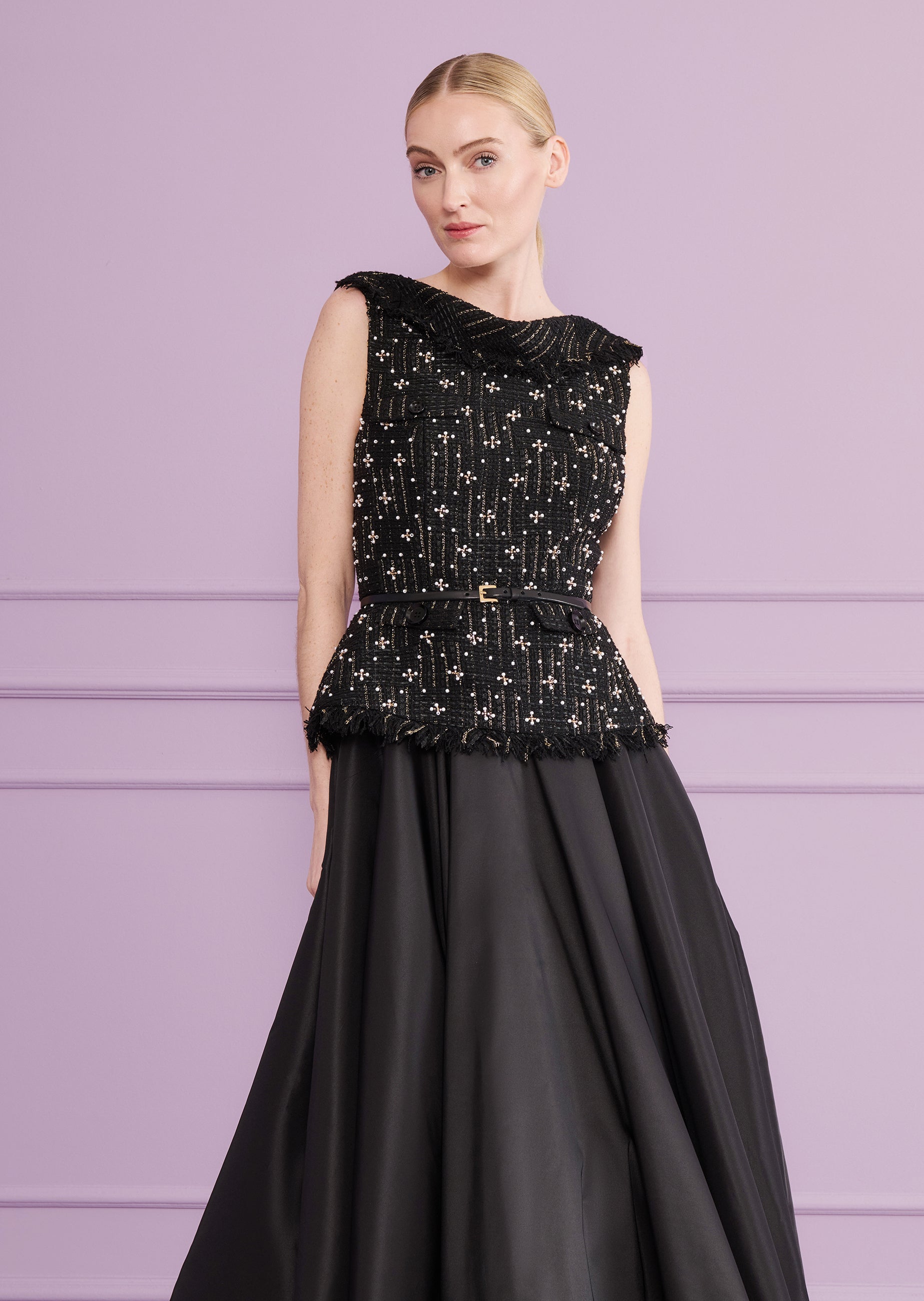 Black sleeveless dress with a beaded and gold-threaded tweed peplum top and a flowing black skirt. Black belt, gold-toned buc
