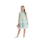 Young girl in a mint green tiered ruffle tulle party dress with a peach bow at the waist, holding a small bouquet of pink roses against a white background.