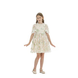 A young girl wearing a champagne-colored knee-length party dress with green and pink floral embroidery and sequins, featuring flutter sleeves and cream t-strap shoes.