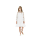 A young girl with long wavy hair wearing a white long-sleeved floral lace dress and matching ballet flats with rose accents, standing against a bright white background.