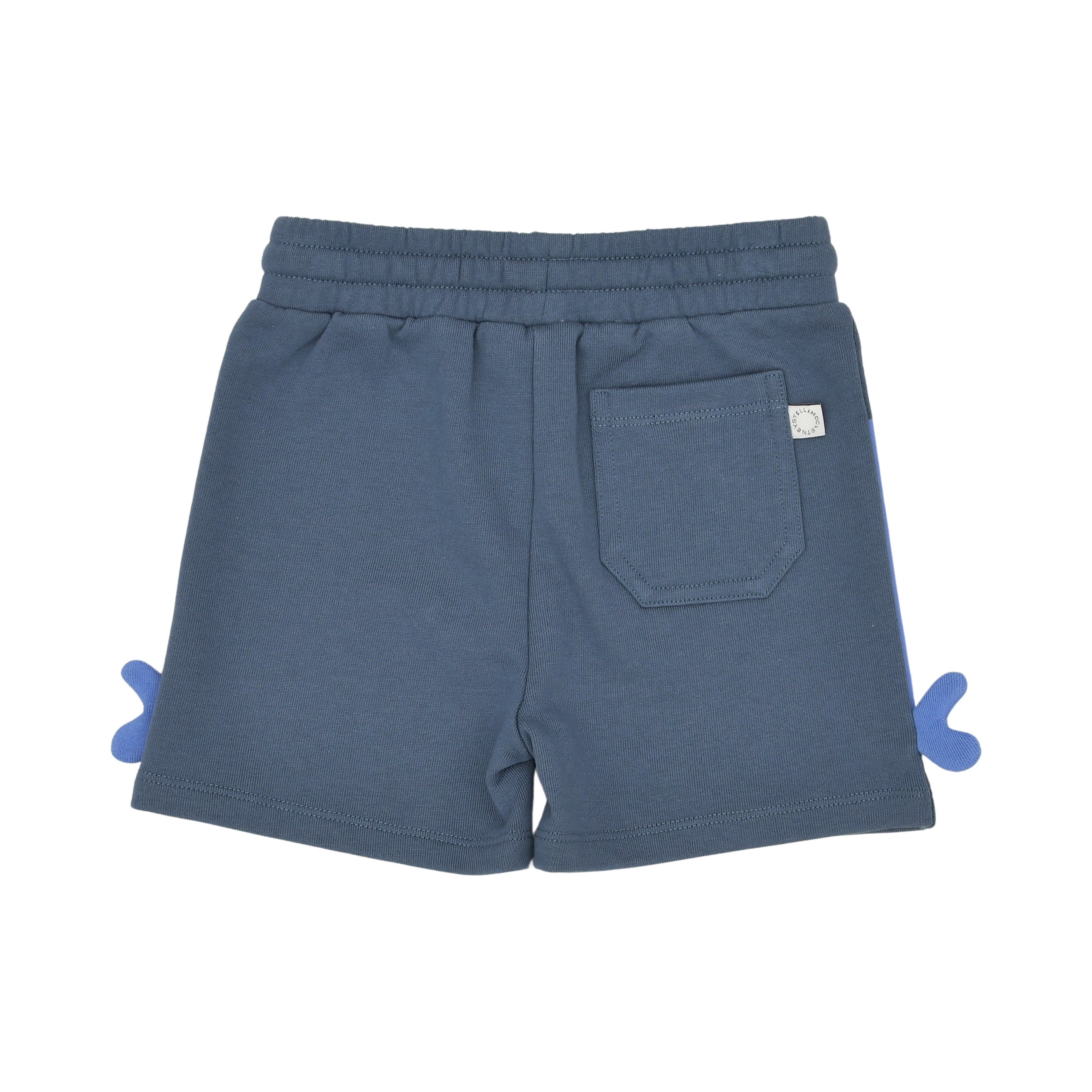 Back view of the Stella McCartney Kids slate blue baby jersey shorts displaying a single right-side patch pocket, side 3D fins, and a white brand logo tag.
