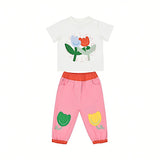 Front full view of a Stella McCartney Kids baby girls two-piece outfit consisting of a white crewneck graphic t-shirt and pink jogger-style trousers on a solid white background.